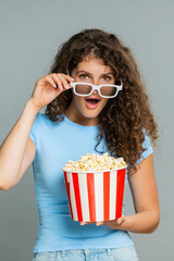 Woman watching exciting thrilling movie film wearing 3D glasses eating popcorn. Emotional surprised...