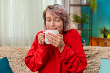 Young woman calmly drinking coffee at home, relaxed, satisfied, expressing peaceful enjoyment and...
