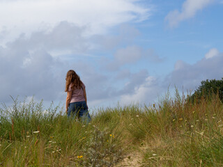 Woman walking alone in coastal dunes for stress relief and mental clarity – perfect for wellness...