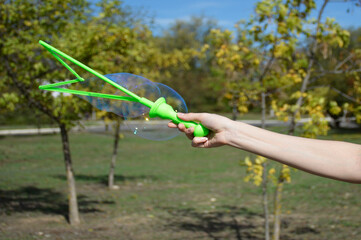 female hand and large soap bubbles. a woman's hand holds a large handle with a soap solution, the wind blows bubbles. fun and entertainment for children. balls shimmer in the sun
