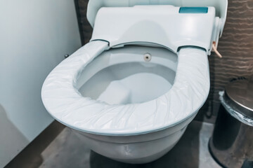 Close up of a toilet with a disposable protective seat cover ensuring hygiene in a public restroom