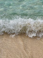 Vertical view of a turquoise wave gently washing onto white sand on Utila Island, Honduras. Minimalist Caribbean beach scene with water, foam, and sand textures.