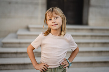 Portrait of smiling blond girl posing with hands on hips on steps