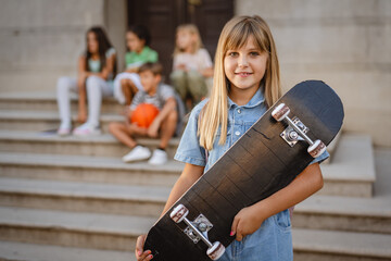 Smiling schoolgirl holding skateboard posing after school