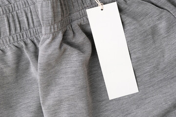 White rectangular paper hang tag on new gray sporty clothing. Top view of blank white price tag...