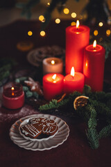 Beautiful elegant table decoration with red candles, fir tree branches with handmade craft toys in the living room. Cozy home atmosphere, holiday aesthetics, atmospheric lights, gingerbread cookies