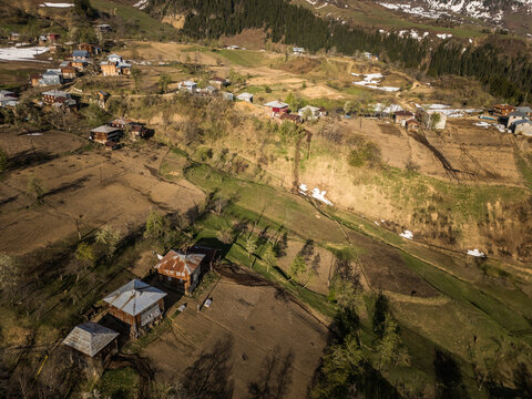 Aerial view of rustic buildings nestled amidst verdant fields and shadowed slopes, where patches of snow linger under the gaze of the distant hills, Gorgadzeebi, Adjara, Georgia.