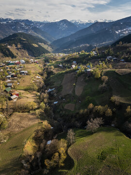 Aerial view of a lush valley carved by a winding stream, nestled among rolling hills and distant, snow-capped peaks, Gorgadzeebi, Adjara, Georgia.