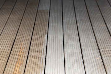 Close up view of a wooden deck featuring parallel planks with visible grooves, subtle color variations, and natural wear patterns under soft lighting.
