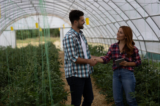 Male and female farmers shaking hands in greenhouse - Powered by Adobe