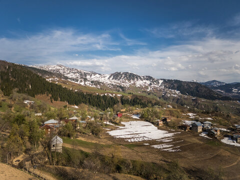 Aerial view of a village nestled in the foothills of snow-capped mountains, where patches of snow linger amidst the awakening spring landscape, Gorgadzeebi, Adjara, Georgia.