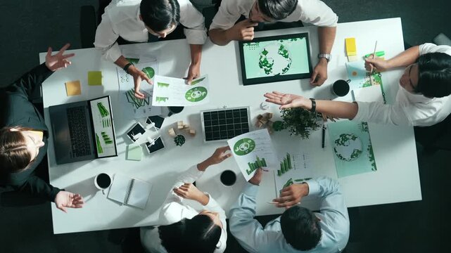 Top down view of business team discussing about using clean energy and sustainable investment at meeting table with wind mill, document with environmental graph and wooden house model. Alimentation.