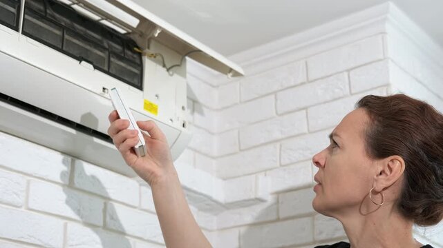 Female with controller by broken conditioner. A view of frustrated female try to turn on the broken air conditioner in the room
