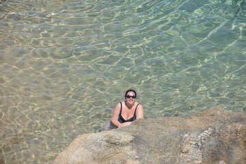 Mid adult woman is posing in transparent clear sea water.