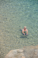 Elderly woman is posing in transparent clear sea water.