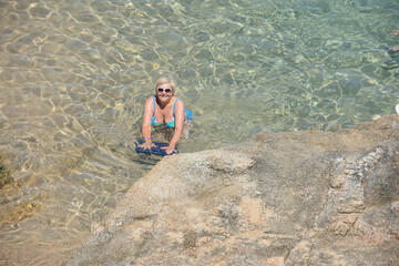 Elderly woman is posing in transparent clear sea water.