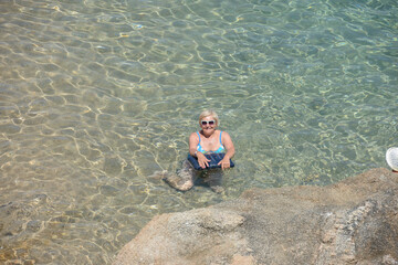 Elderly woman is posing in transparent clear sea water.