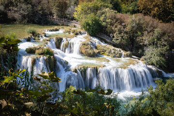 Fototapeta premium Peaceful waterfall in a Croatian national park surrounded by lush greenery and clear water. A stunning natural landscape ideal for travel, nature, adventure, and outdoor-themed content.