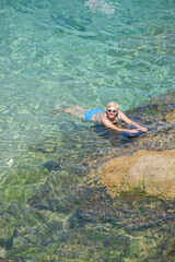 Elderly woman is posing in transparent clear sea water.