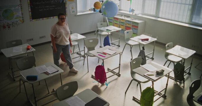 Tired Female Teacher Sitting Alone in Empty Classroom, Relaxing After Class. Woman Feeling Stress, Burnout and Mental Exhaustion in Educational Environment, Working in Elementary School. High Angle.