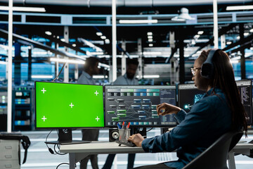 Woman in data center using green screen computer to check for server performance issues. IT expert at work in server room fixing errors slowing down hardware using chroma key PC