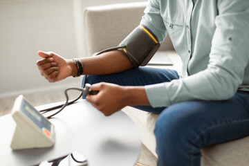 Obraz premium Unrecognizable African Guy Measuring Arterial Pressure Having Hypertension Sitting On Sofa At Home. Cropped. Health Problem With Low And High Blood Tension, Blood-Pressure Checkup. Selective Focus