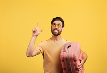 A middle aged man dressed casually holds a pink suitcase while smiling. He appears to be excited,...