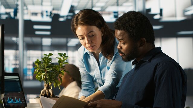 Employee in office receiving project paperwork from management, starting work on new project. Manager giving tasks to worker, providing necessary documents folder, camera A