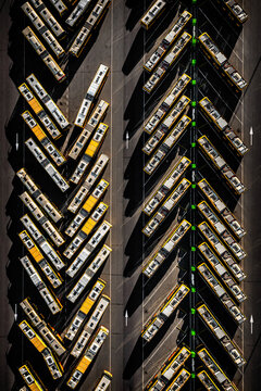Aerial view of rows of yellow buses parked neatly, their shadows creating stark lines on the asphalt, an organised urban landscape unfolds., Poland.