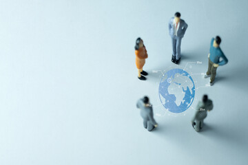 Miniature business people figures in a meeting around a virtual globe. A concept for global business, international strategy, globalization, worldwide teamwork, and corporate management.