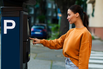 Young woman paying for parking, using outdoors electronic pay station terminal, lady driver using...