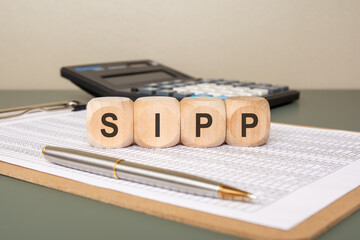 SIPP abbreviation on wooden cubes on a financial spreadsheet with pen and calculator