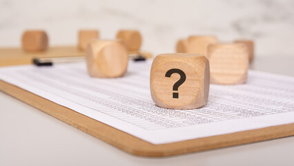 Wooden cube with question mark on financial document, symbol of doubt or inquiry
