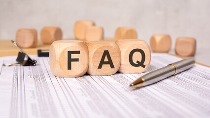 wooden blocks with FAQ letters on financial report sheet and calculator in background