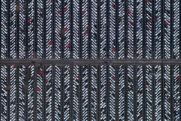 Aerial view of a grid of symmetrical rows of white vehicles with red accents, creating a stark contrast against the dark background, Sweden.