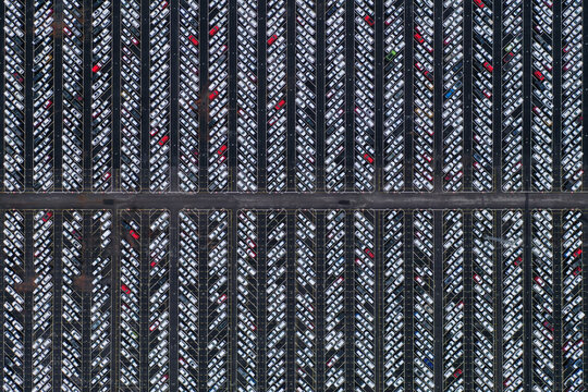 Aerial view of a grid of symmetrical rows of white vehicles with red accents, creating a stark contrast against the dark background, Sweden.