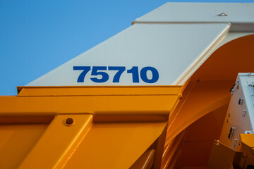 Close-up of yellow and white mining dump truck with marking 75710 against blue sky