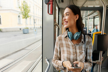 Happy young woman passenger standing in tram near window, enjoying trip at public transport looking at window and smiling