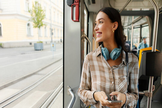 Happy young woman passenger standing in tram near window, enjoying trip at public transport looking at window and smiling