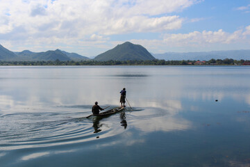 Two fishermen in a long, narrow canoe in a still lake in Myanmar.