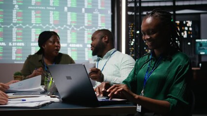Portrait of smiling black analyst preparing a pitch for important meeting, increasing funds for development after hours. Coworkers team attend a discussion to address goal setting. Camera A.