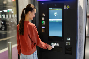 Lady driver paying and taking ticket in parking meter near terminal in the underground parking...