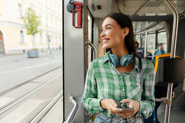 Happy young woman passenger standing in tram near window, enjoying trip at public transport looking at window and smiling