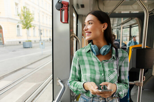 Happy young woman passenger standing in tram near window, enjoying trip at public transport looking at window and smiling