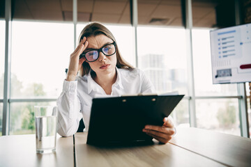 Focused young businesswoman performing analytical review in modern office environment during a work...