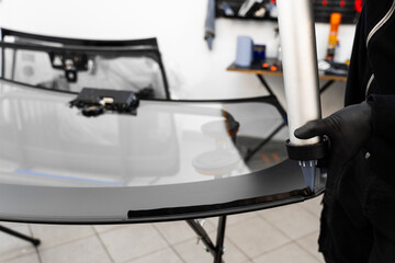 Applying adhesive to a car windshield using a caulking gun. Urethane caulking gun applies flexible adhesive, forming a watertight seal at car windshield replacement.