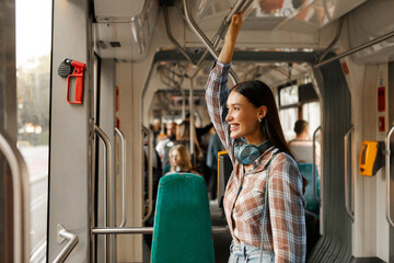 Happy woman passenger standing in modern tram and enjoying comfortable ride in public transport, looking at window and smiling