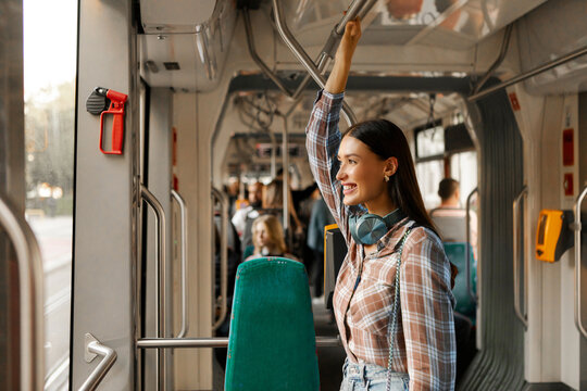 Happy woman passenger standing in modern tram and enjoying comfortable ride in public transport, looking at window and smiling - Powered by Adobe