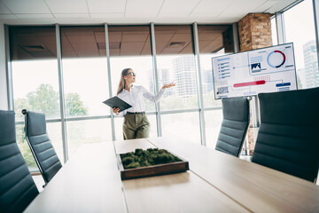 Businesswoman presenting analytics in a modern office setting with glass walls, professional...