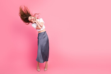 Young woman with flowing brown hair poses joyfully wearing elegant attire on vibrant pink...